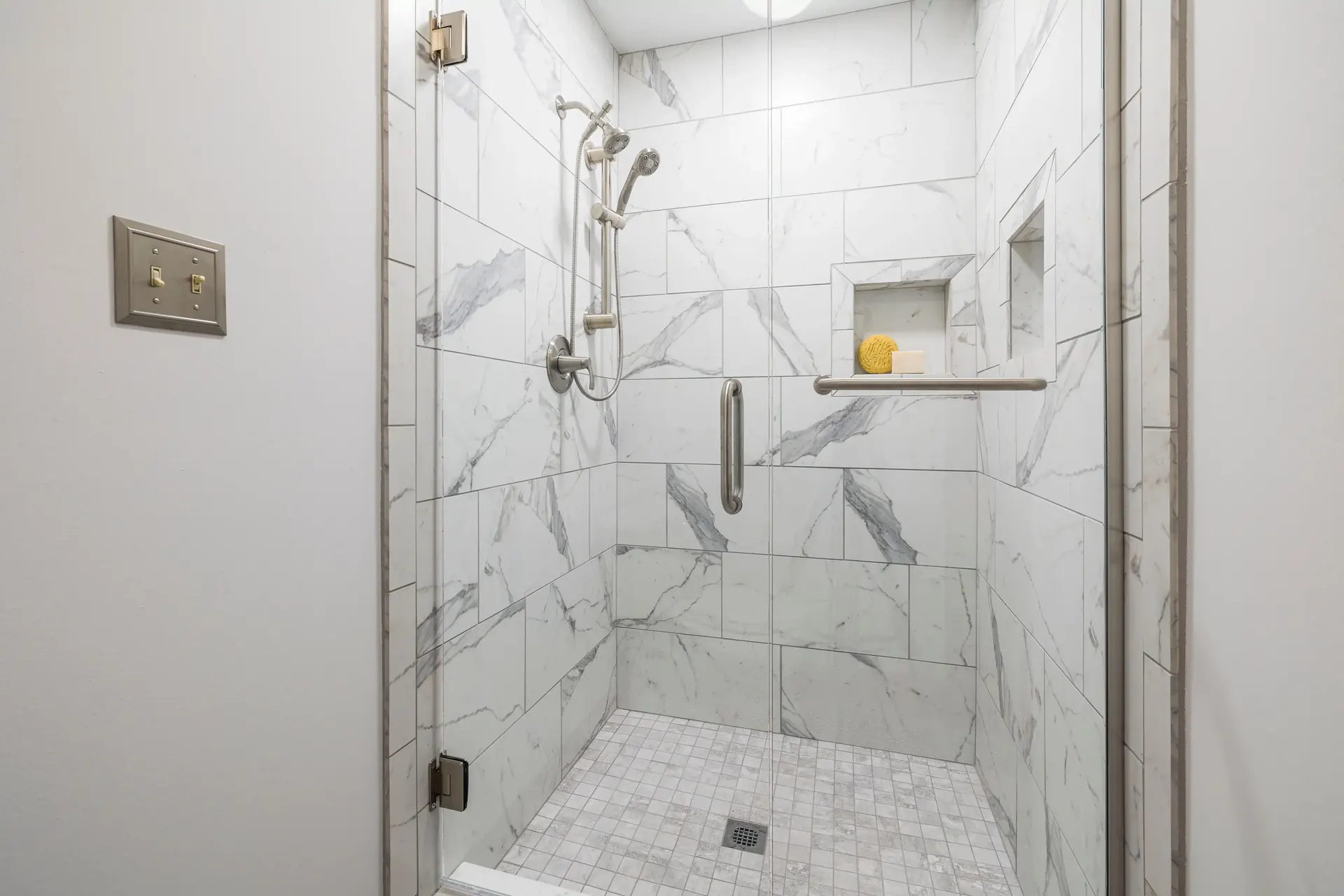 Marble-look tile shower with a niche, glass door and grab bar