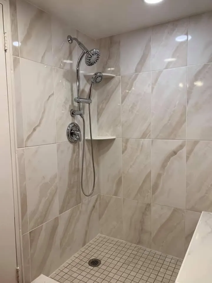 Floor-to-ceiling marble-look porcelain shower with a pebble mosaic floor