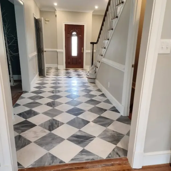 Entry hall with a diagonal checkerboard of white and gray marble-look tile running from the front door past the staircase.