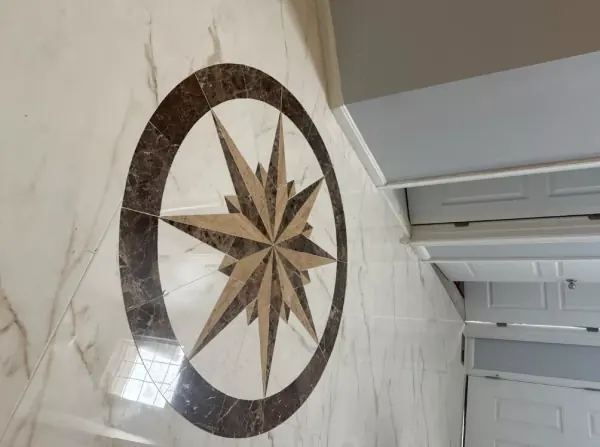 Close view of a compass rose medallion with a dark brown ring and beige star points, set into white veined floor tile.