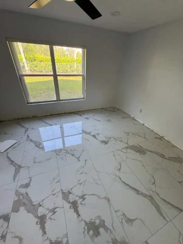 Finished room with large polished white porcelain floor tile with gray veining, a window and a ceiling fan.