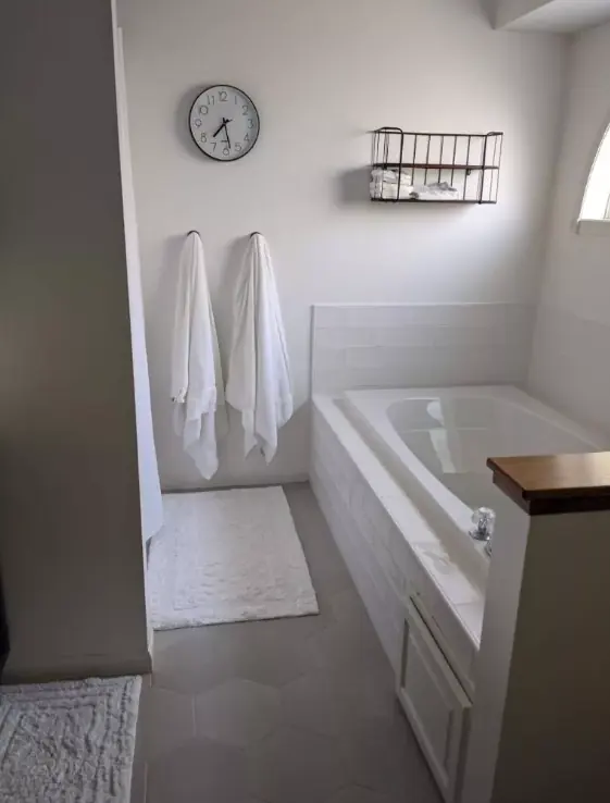 Bathroom with large gray hexagon floor tile, a drop-in tub with a white subway tile surround and white towels on the wall.