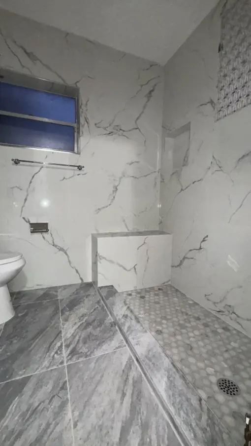 Walk-in shower with white veined wall tile, a low tiled half wall, a light hex mosaic floor and gray floor tile set on the diagonal.
