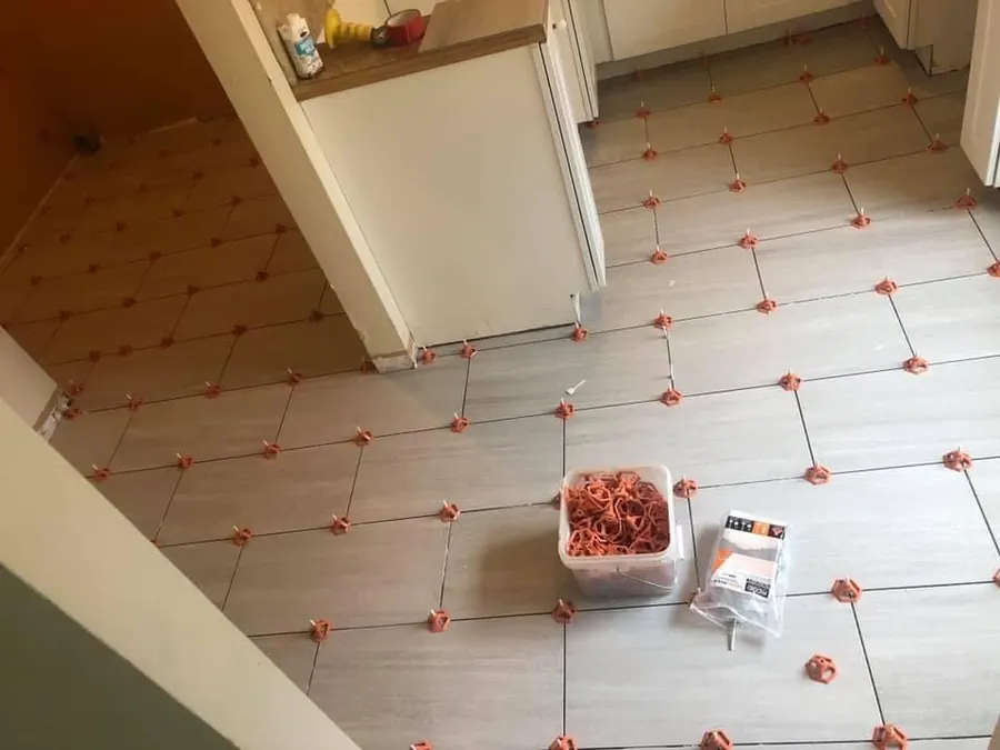 Floor tile being leveled with red leveling clips before grouting